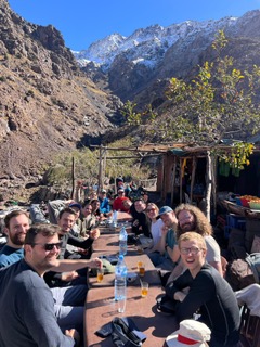 Travelers resting at a rustic mountain stop beneath snow-dusted Atlas peaks